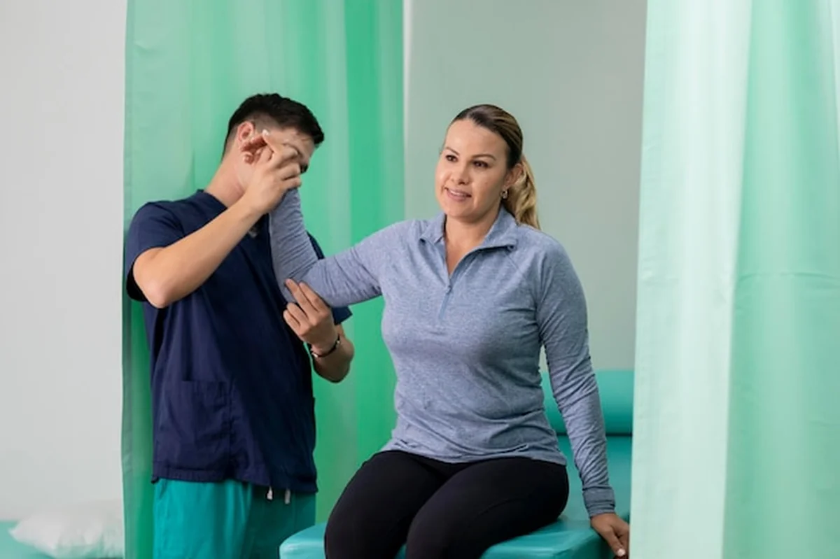 Terapeuta sprawdza ramię Latynoski, która siedzi na stole w biurze