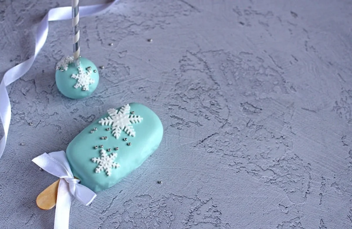 Noworoczne ciasta z płatkami śniegu na patyku na niebieskim tle