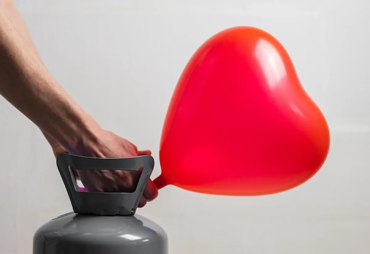 Młody facet nadmuchuje balon helem