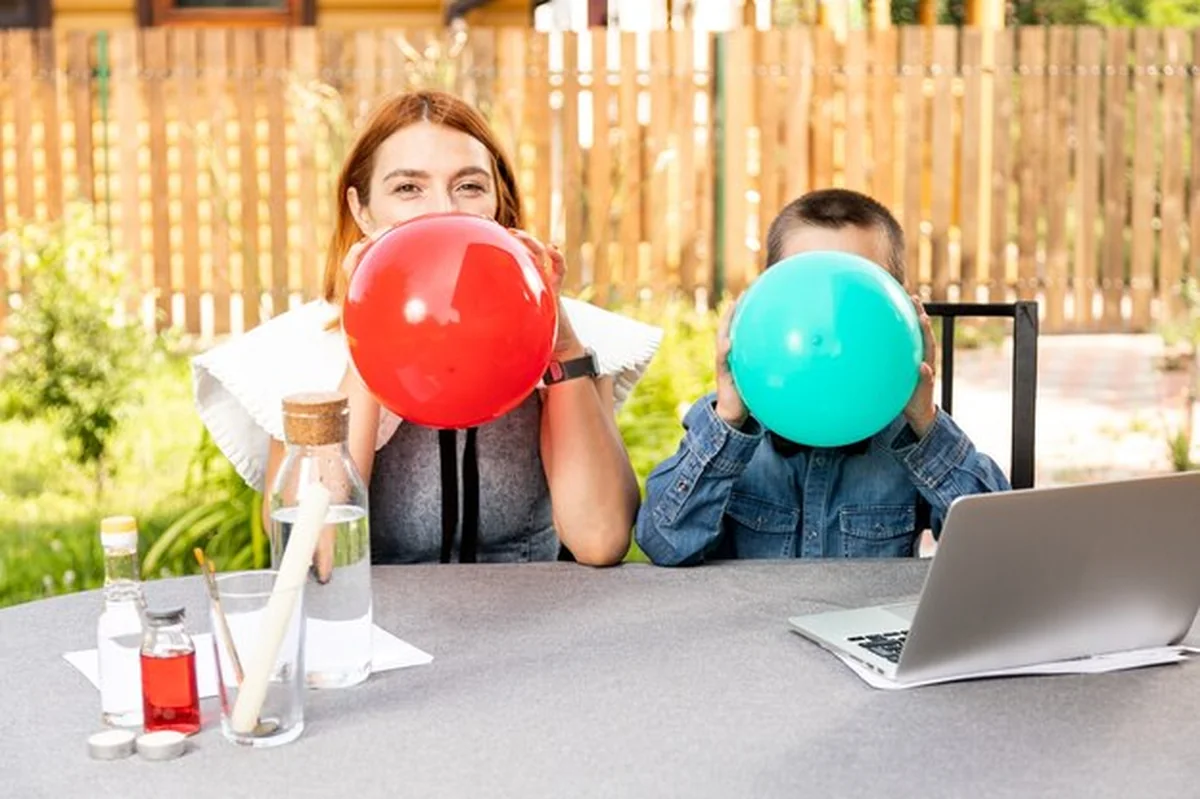 Chłopiec z mamą nadmuchuje kolorowe balony w ogrodzie