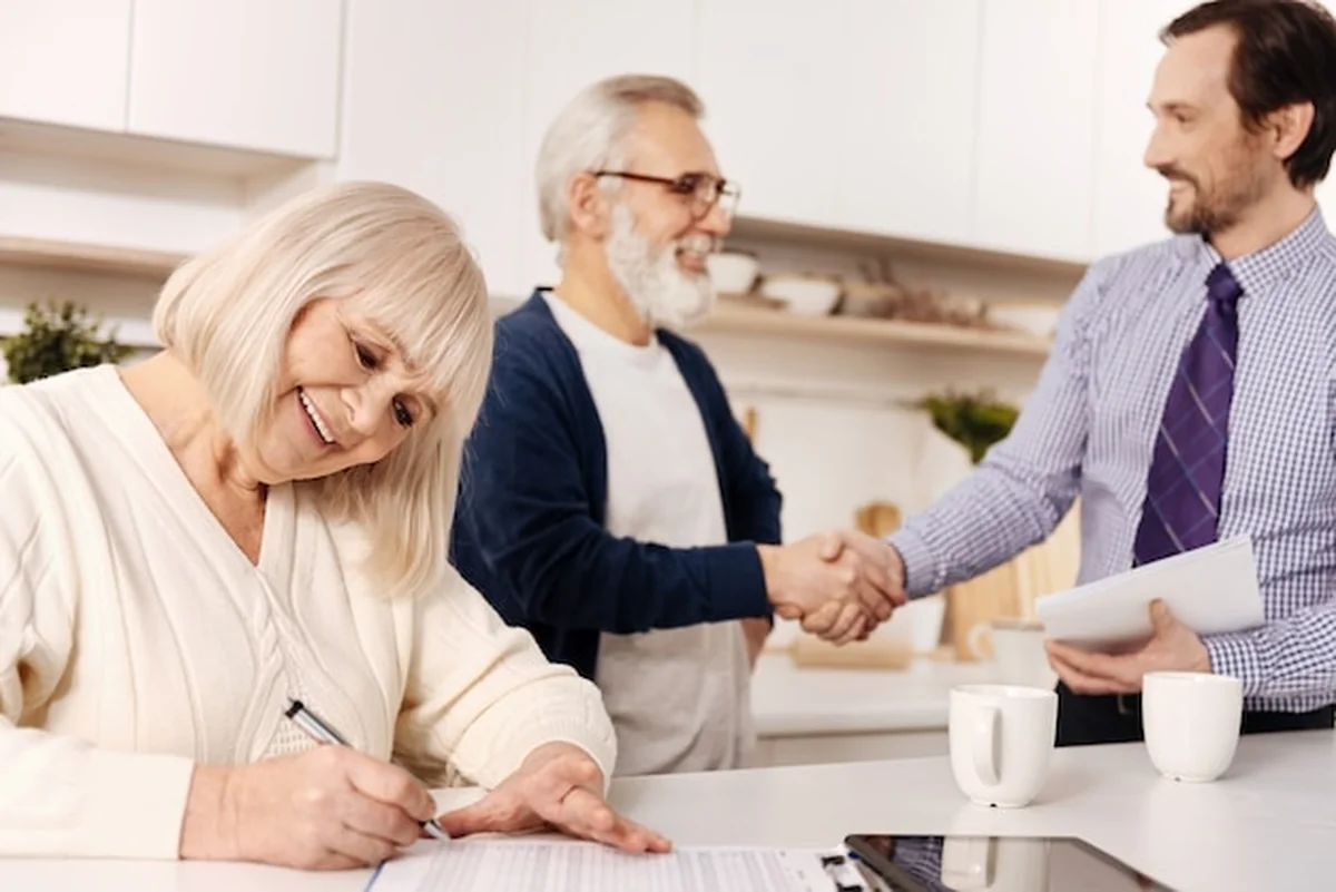 Starsza kobieta podpisuje umowę, a mąż wita prawnika