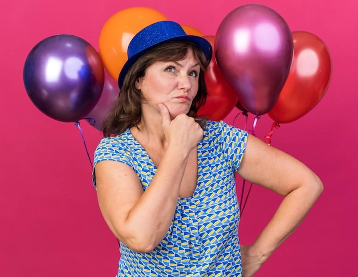 Kobieta w średnim wieku trzymająca kolorowe balony i patrząca w górę