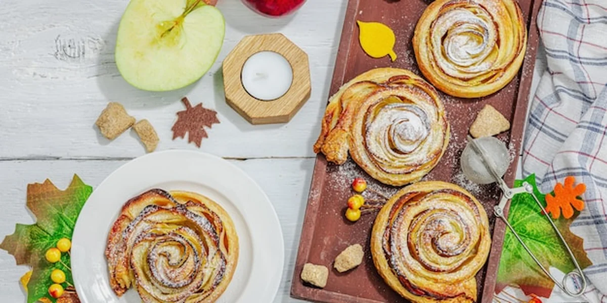 Ciasto z różami jabłkowymi posypane proszkiem cukrowym na drewnianym tle