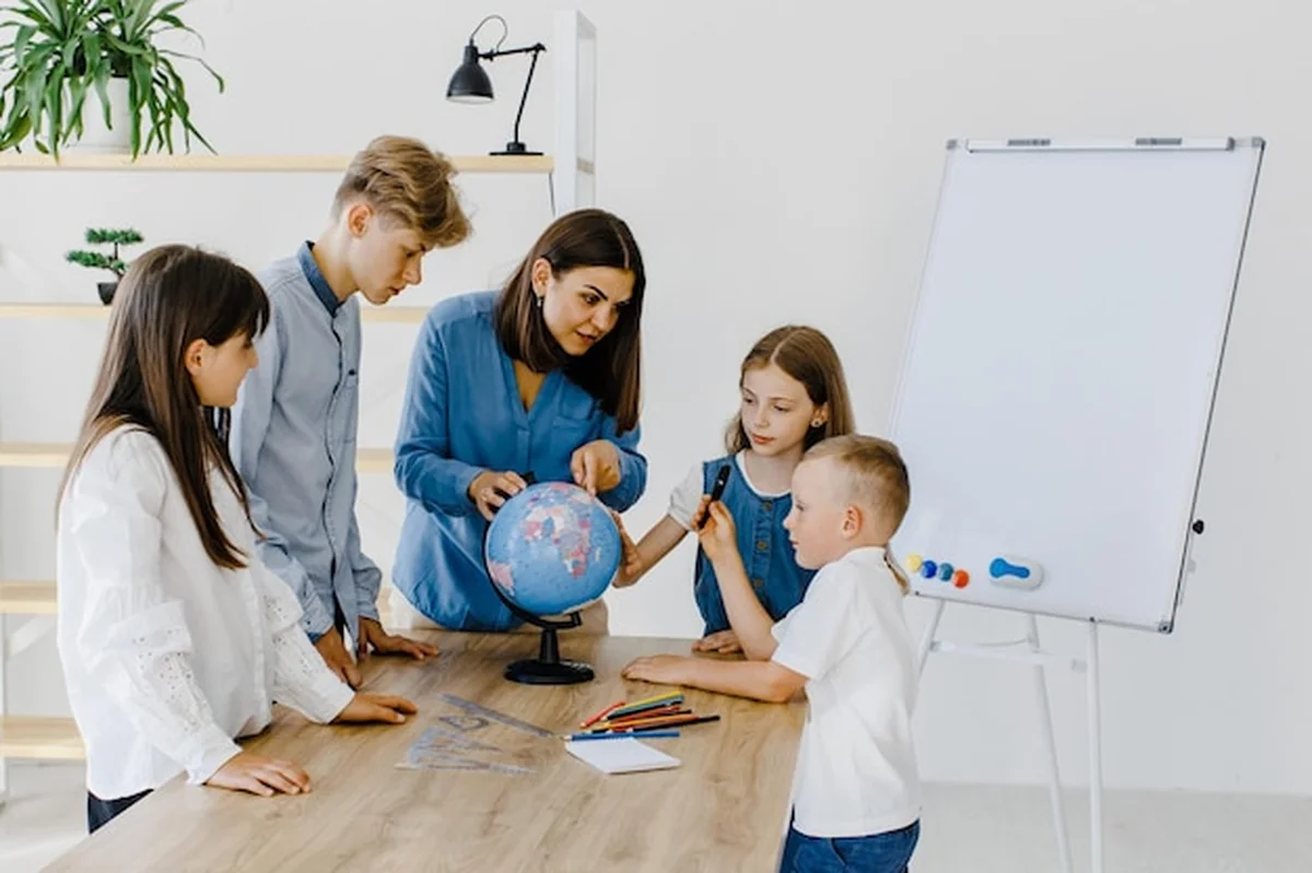 Nauczyciel i dzieci w klasie patrzą na globus, nauczyciel pomaga wyjaśnić lekcję dzieciom przy biurku