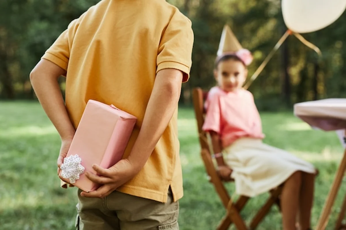 Chłopiec ukrywający prezent na przyjęciu urodzinowym na świeżym powietrzu