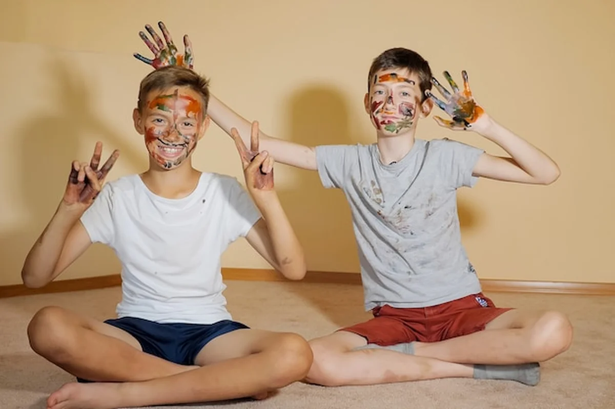 Nastoletni chłopcy siedzący na podłodze z farbami, patrzący w kamerę