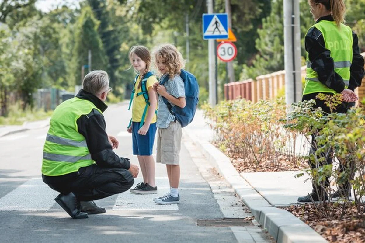 Policjant kuca przed pieszym, ucząc dzieci przechodzenia przez jezdnię