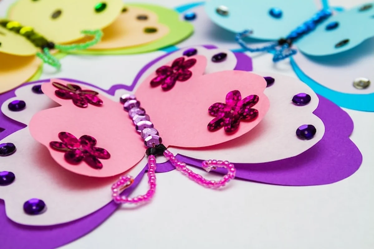 Trzy motyle z papieru i cekinów na aplikacji klejonej gorącym pistoletem