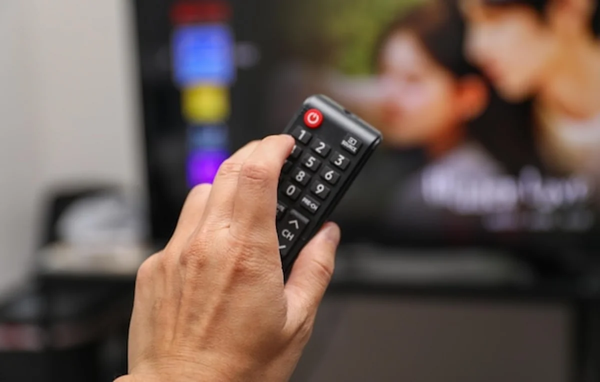 Ręka trzymająca zdalne sterowanie obok eleganckiego urządzenia