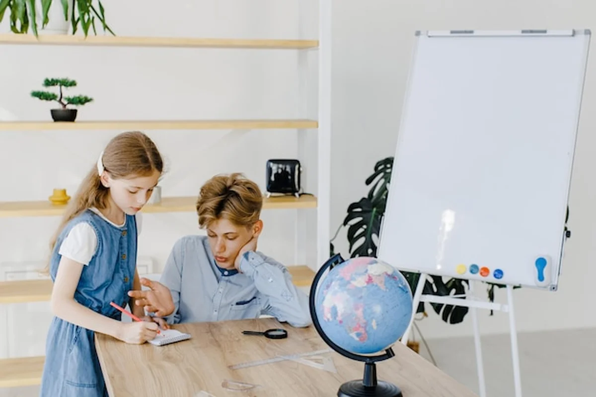 Nastoletnia dziewczyna i chłopiec robią projekt z kulą ziemską w klasie