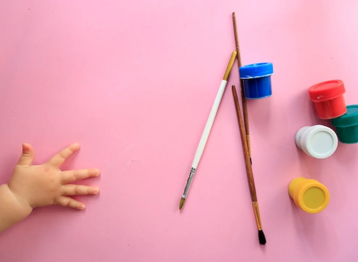 Ręka dziecka trzymająca pędzle i malująca obrazek z góry